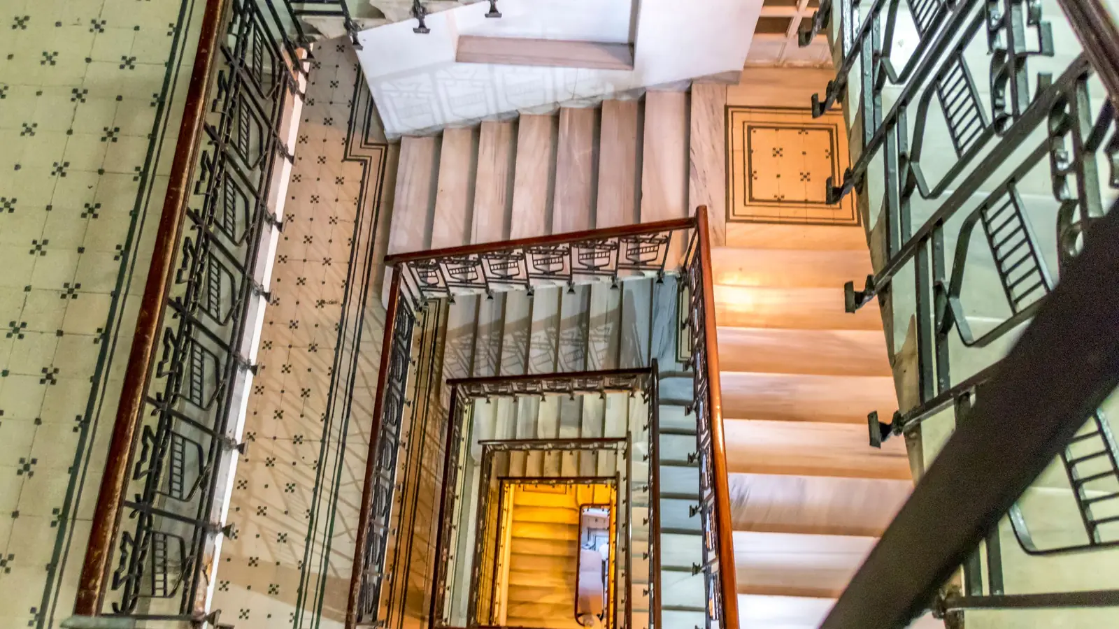 Cage d'escalier d'immeuble ancien vue d'en haut, rampe en fer forgé et murs carrelés