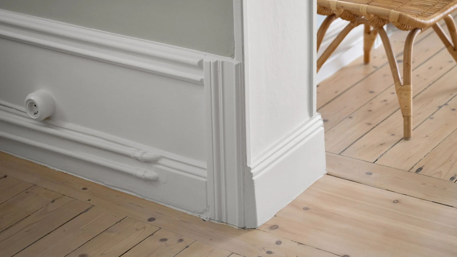 Plinthe moulurée blanche et parquet clair au pied d'un mur